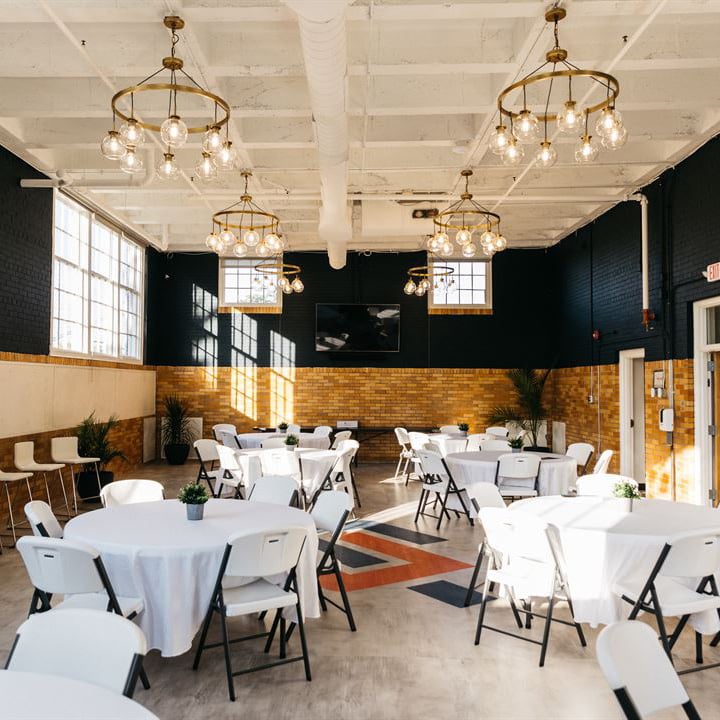 A large open space with beautiful lighting and white round tables